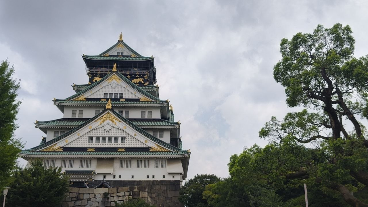 Fachada del Castillo de Osaka con arboles y cielo nublado