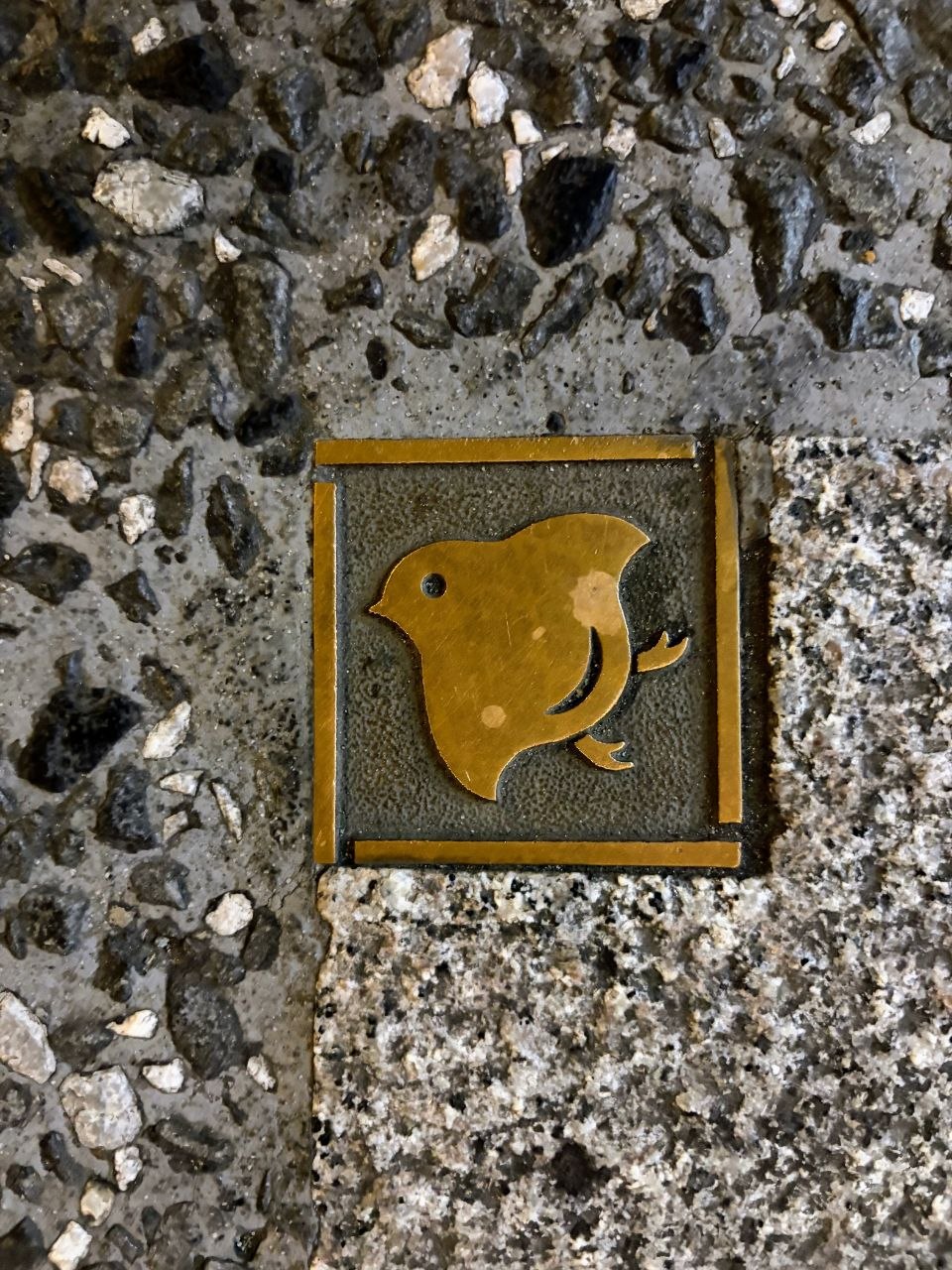 Placa dorada con silueta de pajaro incrustada en el suelo de Pontocho