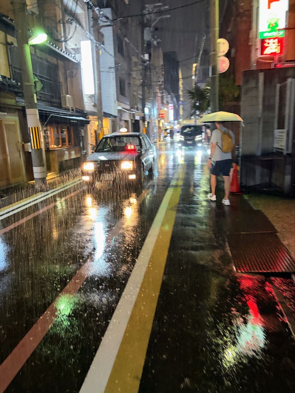 Calle de Kyoto de noche bajo lluvia intensa con taxi y luces reflejadas