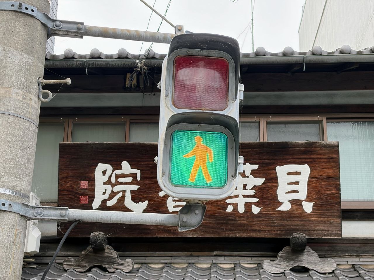 Semaforo peatonal verde frente a un cartel de madera en Kyoto